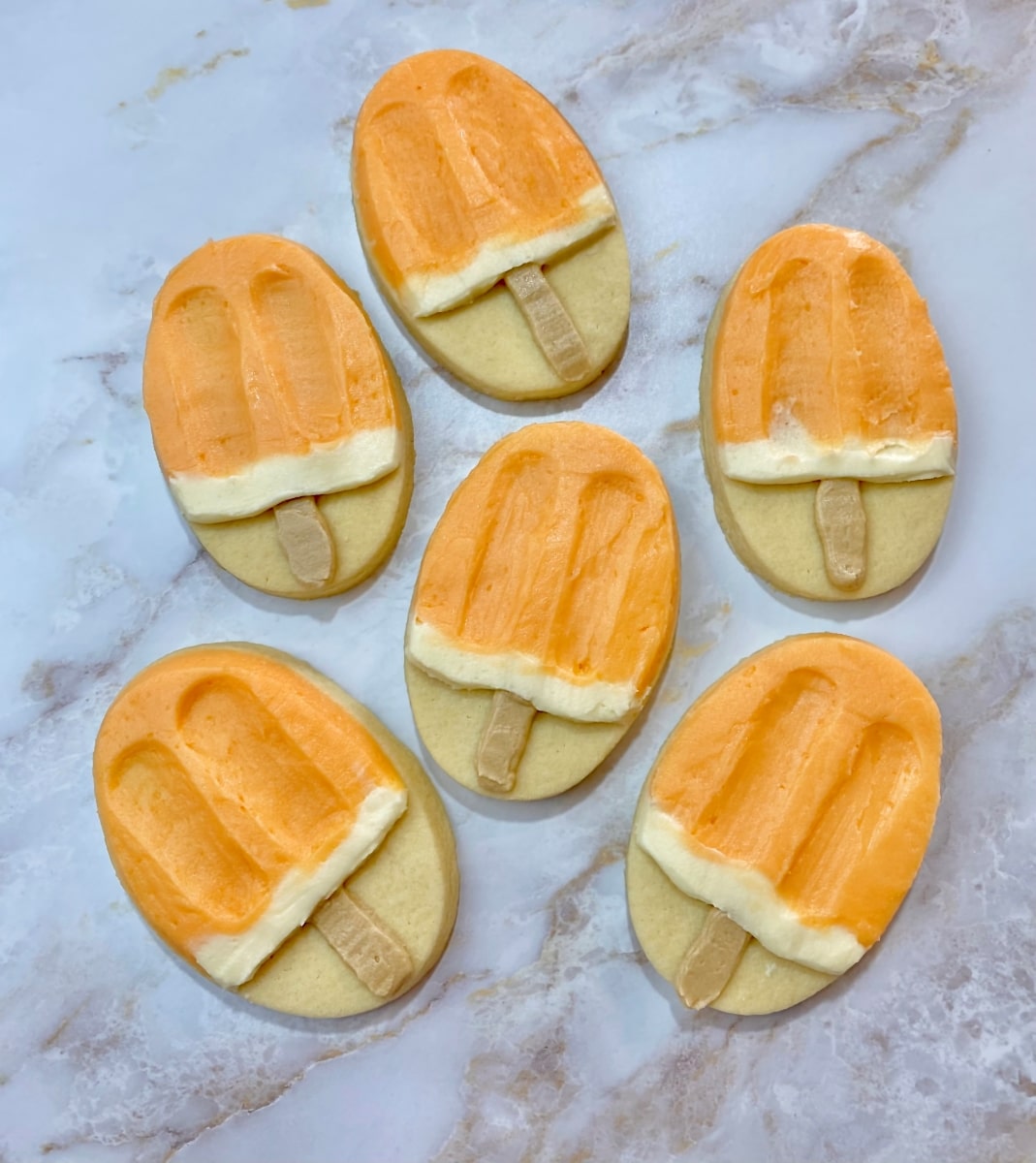 sugar cookies decorated like creamsicles with orange flavored buttercream frosting